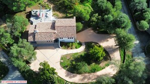 Vista aérea de una casa con techo de tejas, rodeada de vegetación y un camino de entrada curvo.