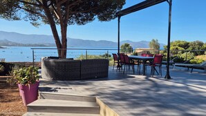 Una terraza con mesa y sillas, un rincón de descanso con mobiliario de mimbre y vistas al mar y a las montañas.