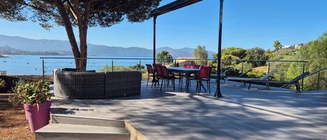 A terrace with a table and chairs, a wicker seating area, and a view of the sea and mountains.