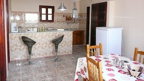 Une cuisine compacte avec deux tabourets de bar, une table à manger recouverte d’une nappe à motifs et un réfrigérateur.