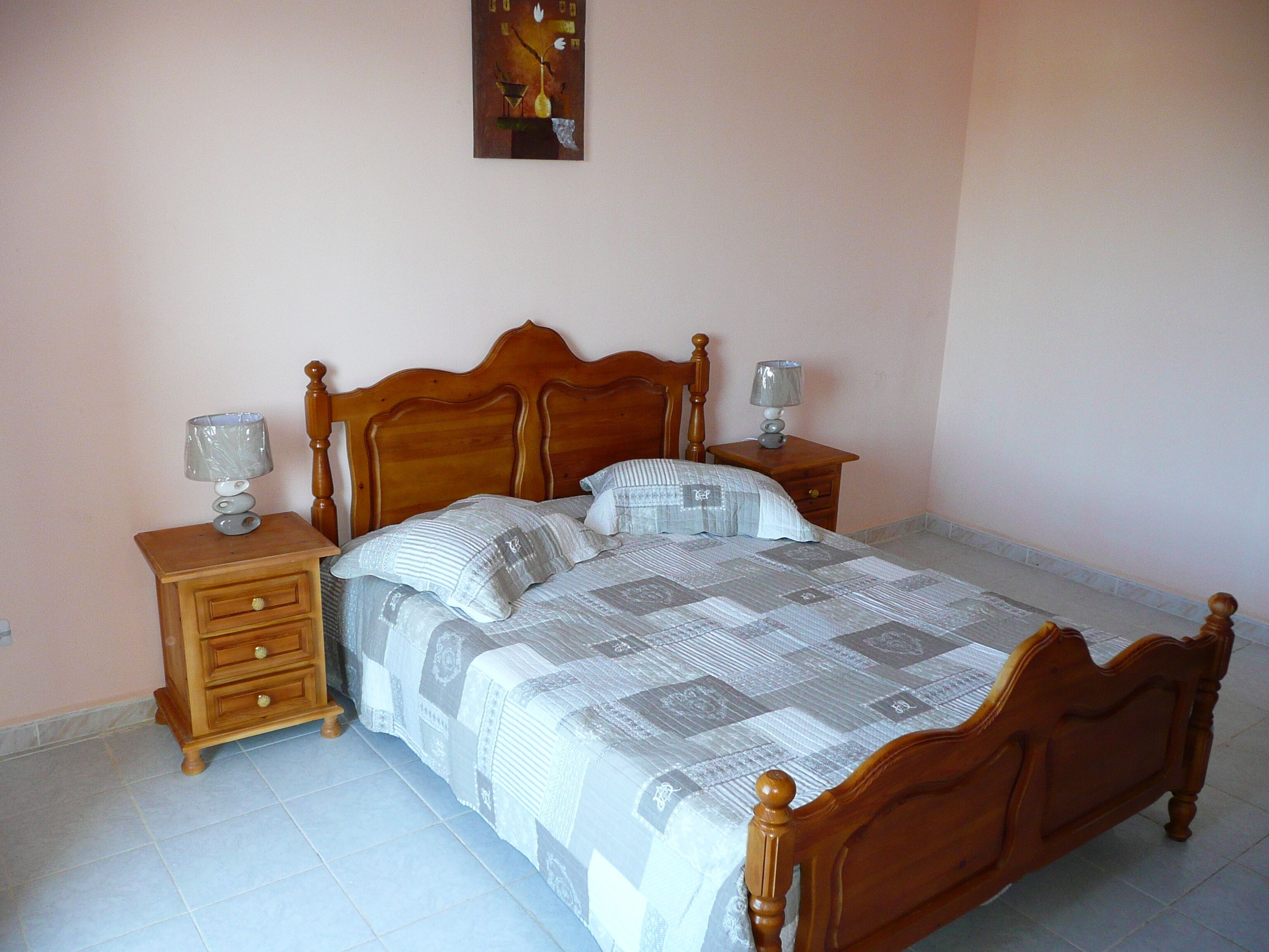 A bedroom with a wooden bed, two bedside tables, and a nightstand.