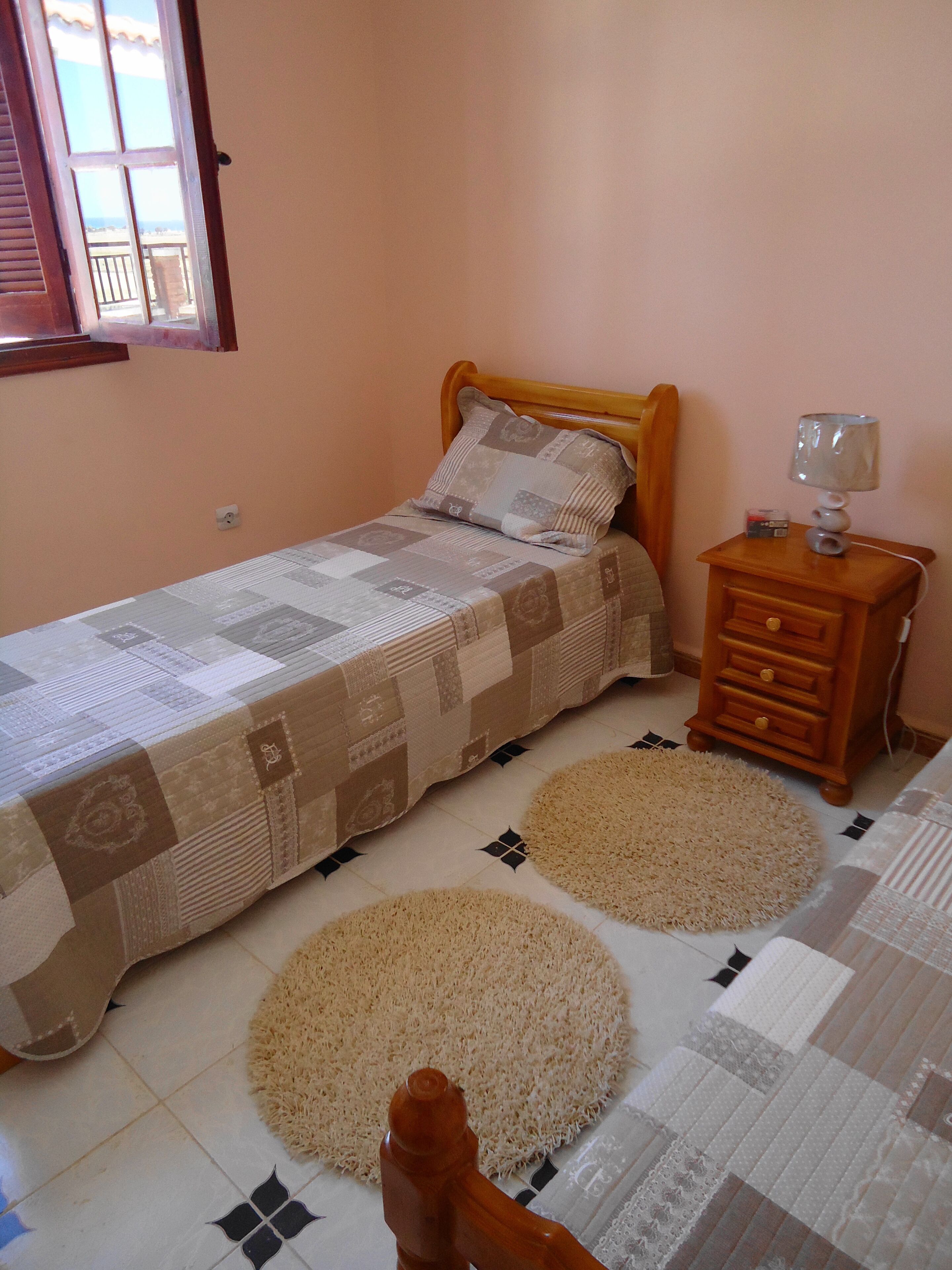 Een kleine slaapkamer met een enkel bed, een nachtkastje en twee vloerkleden.