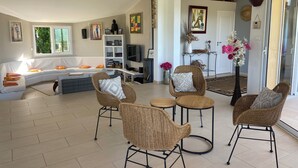 Un salon avec un canapé, des fauteuils en osier, un téléviseur et une bibliothèque.