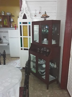 A corner room with a dining table, a wooden cabinet with glass doors, and a white cabinet with a decorative top. - Casa El Mirador - Yliana (Baracoa)