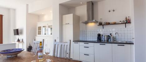A modern kitchen with white cabinets, a wooden dining table, and a hanging light fixture.
