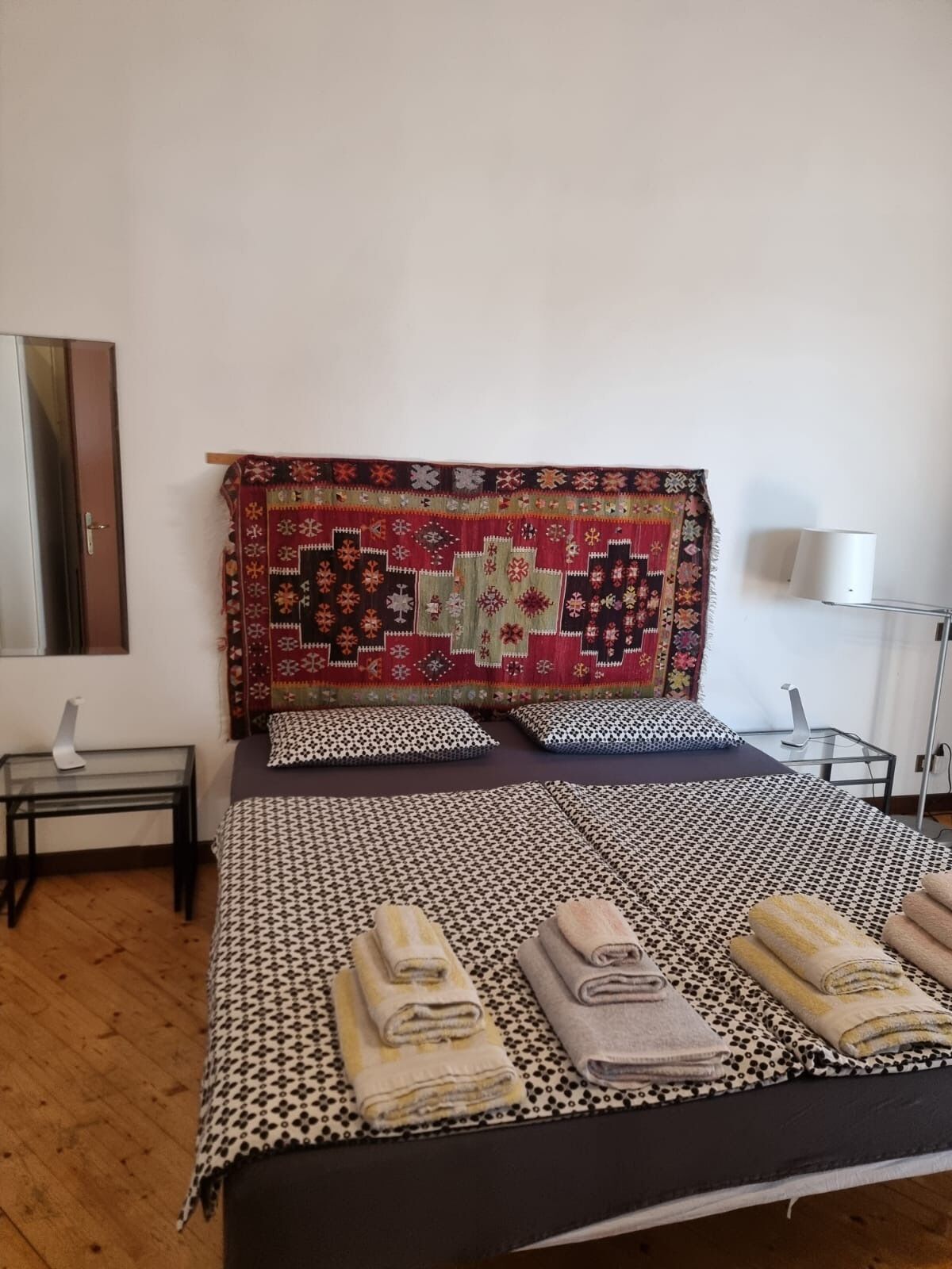 Un lit bien fait, avec une literie à motifs, une tête de lit ornée d’une courtepointe décorative et une table de chevet avec une lampe.