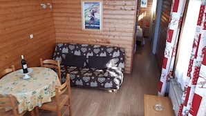 A cozy wooden cabin interior with a dining area, a sofa with a heart-patterned cover, and a poster on the wall. - T2 apartment in FONT ROMEU. Label 2 Clévacances. Exceptional panorama (Font-Romeu-Odeillo-Via)