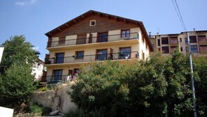 A multi-story building with balconies, a stone base, and surrounding greenery. - T2 apartment in FONT ROMEU. Label 2 Clévacances. Exceptional panorama (Font-Romeu-Odeillo-Via)