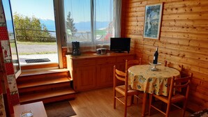 A cozy cabin with a wooden interior, a dining table with chairs, a small kitchen area with a stove and a TV, and a view of the mountains through the window. - T2 apartment in FONT ROMEU. Label 2 Clévacances. Exceptional panorama (Font-Romeu-Odeillo-Via)
