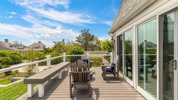 A deck with outdoor furniture, a glass door leading to a covered area, and a view of surrounding houses.