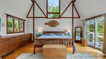 A bedroom with a wooden bed, a large window, and a view of greenery outside.