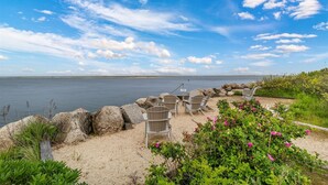 A beachside seating area with chairs and a table, overlooking a calm body of water.