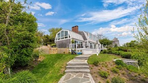 A modern house with a stone pathway leading to the entrance, surrounded by lush greenery and a clear sky.