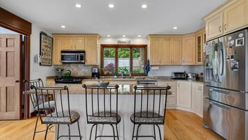 Una cocina amplia con armarios de madera, un refrigerador de acero inoxidable, un ventanal grande y una zona de bar con taburetes.