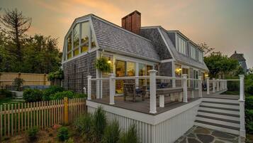 A modern house with a large deck, a brick chimney, and a stone pathway leading to the entrance.