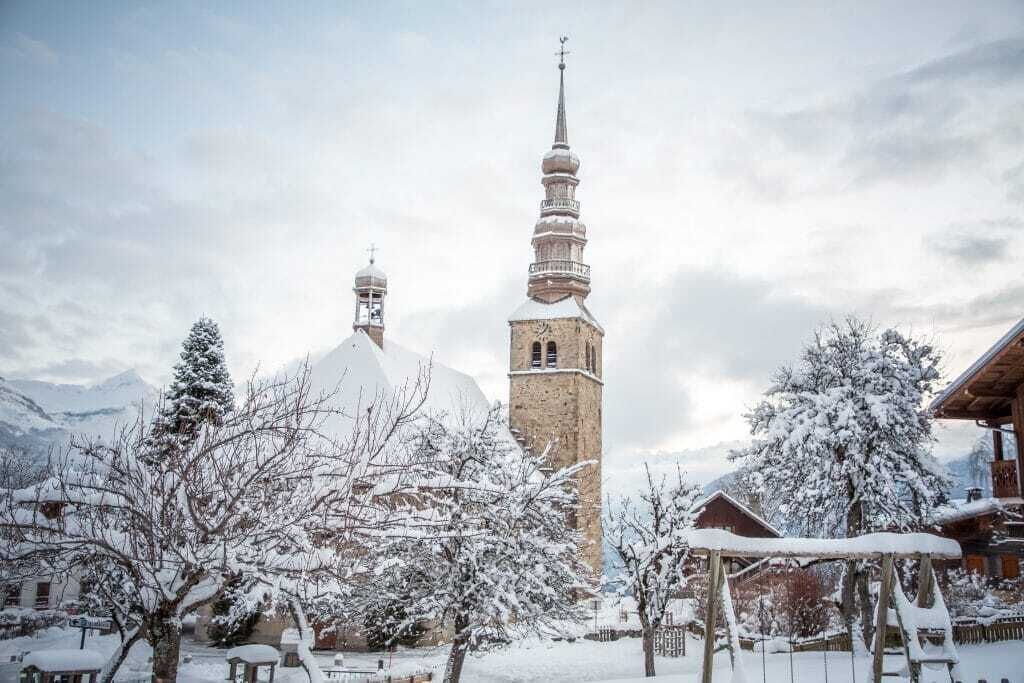A snowy village with a prominent church featuring a tall bell tower and a dome.