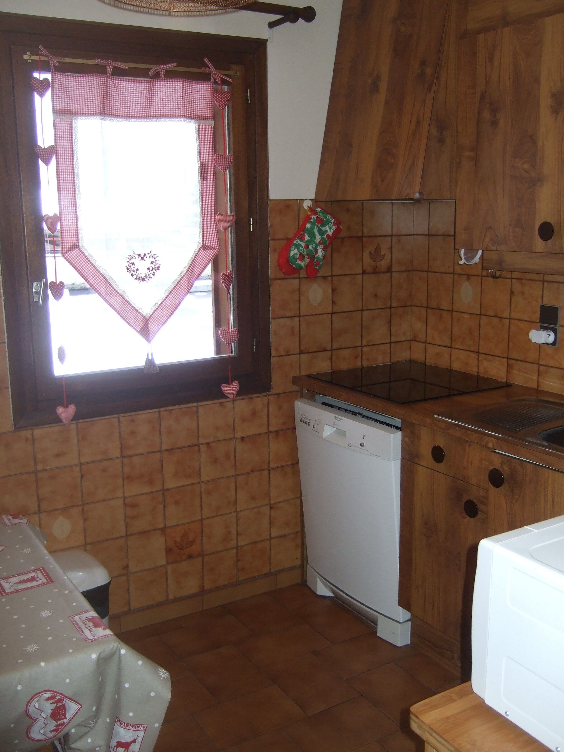 Een keuken met een houten kast, een vaatwasser en een raam met een geruit gordijn.