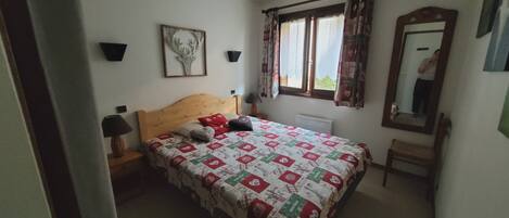 Et soveværelse med en seng, et natbord, en lampe, et vindue med gardiner, et spejl og et billede hængende på væggen.