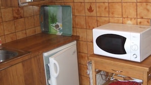 Cuina compacta amb microones, nevera petita i armari de fusta.