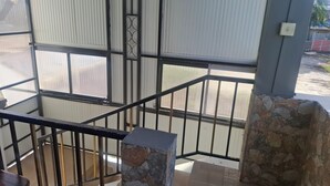 Un balcón con barandilla de metal, pilares de piedra y vistas a un estacionamiento.