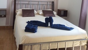 Una cama bien tendida con estructura de metal, un ventilador de techo y un equipo de aire acondicionado en la pared.