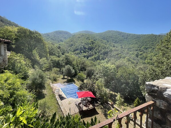 Ein Poolbereich mit einem roten Sonnenschirm, umgeben von üppiger Vegetation und Bergen im Hintergrund.