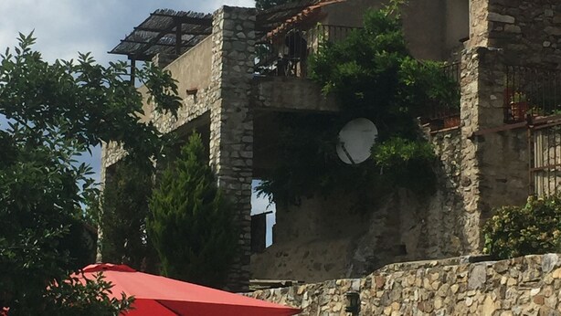 Un edificio de piedra con techo rojo, una antena parabólica y un muro de piedra.