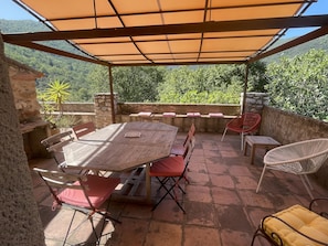 Eine Terrasse im Freien mit einem Holztisch und -stühlen, einer Steinmauer und Blick ins Grüne.