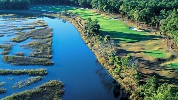 Ein Golfplatz mit einem Wasserhindernis und dichtem Wald.