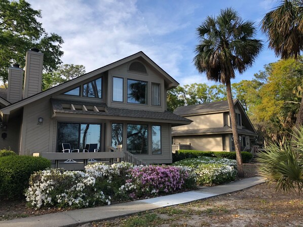 A two-story house with large windows, a covered porch, and a well-maintained garden with various flowering plants. - DATAW ISLAND - 3/2 Waterfront Villa with Bicycles and Grill (Saint Helena Island)