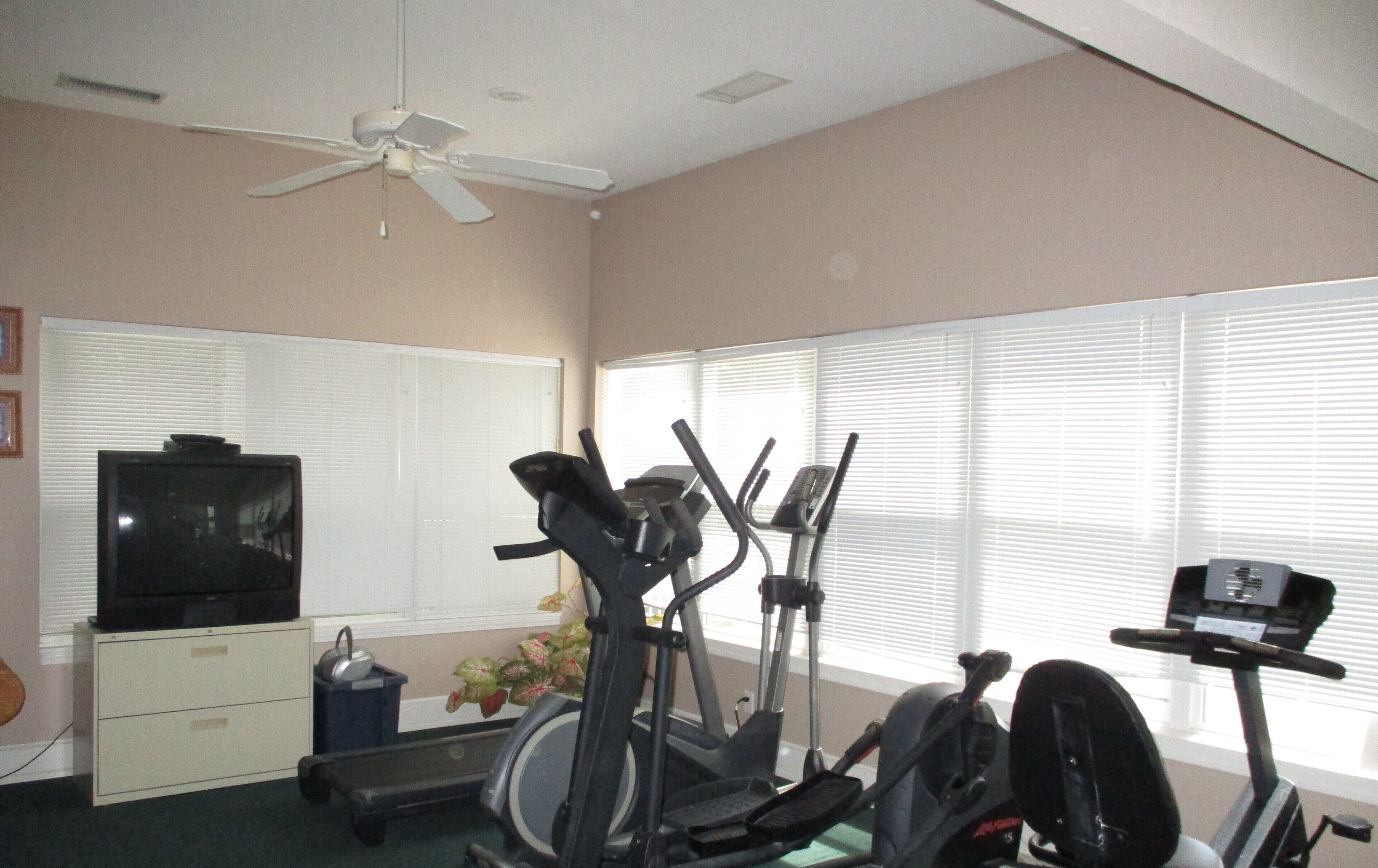 Un gimnasio en casa con equipo de ejercicio, un televisor y un ventilador de techo.