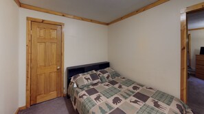 A bedroom with a wooden door, a bed with a patterned blanket, and a dresser.