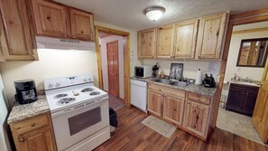 A compact kitchen with wooden cabinets, a stove, a microwave, and a dishwasher.
