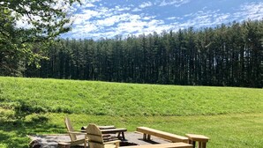 Een picknickopstelling met banken en stoelen in een grasveld, met een bos op de achtergrond.