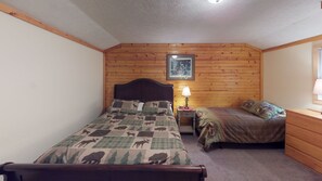 Une chambre avec deux lits, des lambris en bois sur les murs, une table de chevet avec une lampe et un tableau encadré au-dessus de la tête de lit.