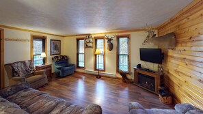 A living room with a fireplace, a television, and a deer head mounted on the wall.