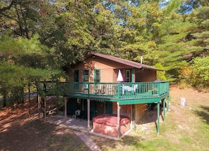 A cabin with a green balcony, a covered outdoor seating area, and a hot tub.