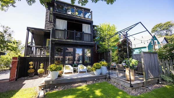 A two-story house with a balcony, outdoor seating area, and a wooden deck.