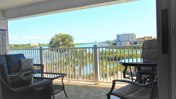 A balcony with wicker furniture and a view of a body of water and buildings. - Waterfront Condo with an amazing view - Pet Friendly (Indian Shores)