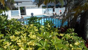 A pool area with a white fence, lounge chairs, and a building in the background. - Waterfront Condo with an amazing view - Pet Friendly (Indian Shores)
