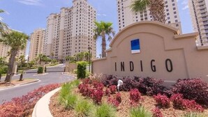 A residential area with a sign reading "INDIGO" and tall buildings in the background. - Indigo 504E BeachFront!Bonus Den,Best View&Amenities HUGE Pool!HotTub Pickleball (Pensacola)