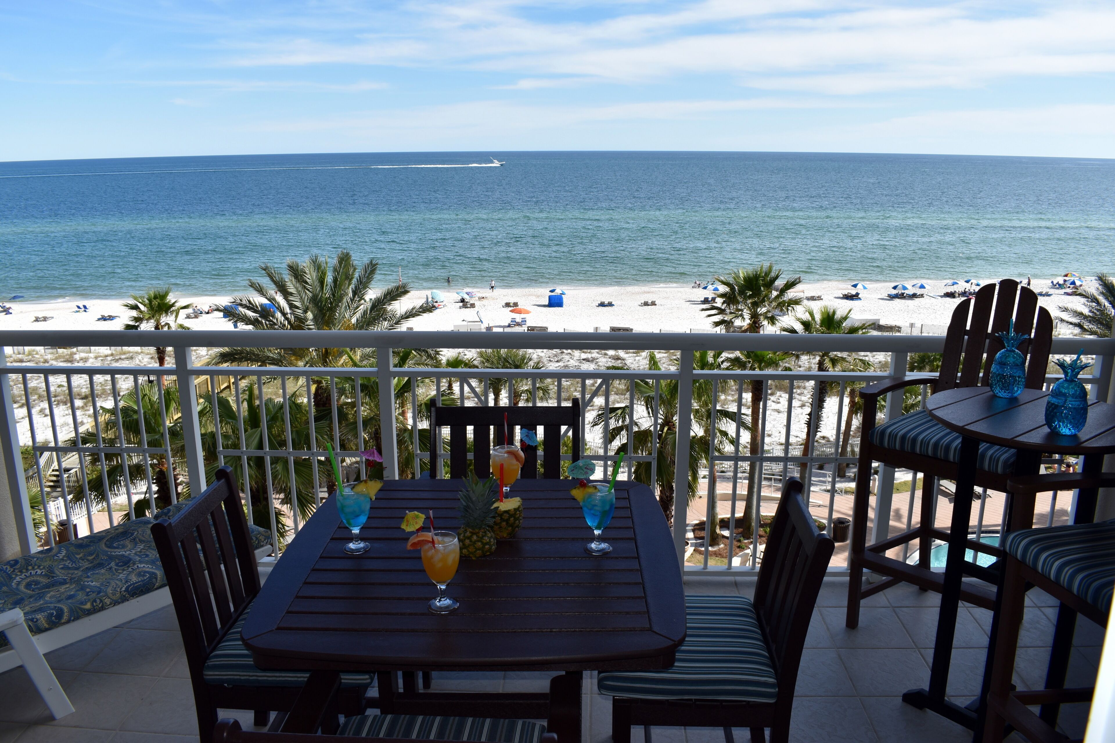 Ein Balkon mit Tisch für zwei Personen, mit Blick auf einen Strand mit Sonnenschirmen und Palmen.