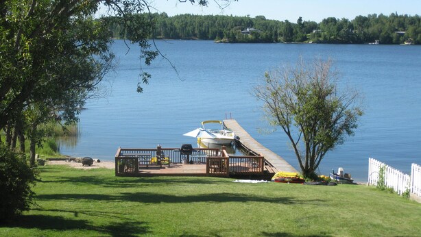 Terraza junto al lago con un bote, parrilla y asientos al aire libre.