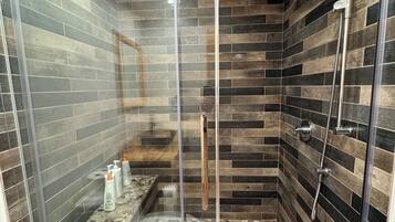 A glass-enclosed shower with a pebble-tiled floor and a wooden wall design.