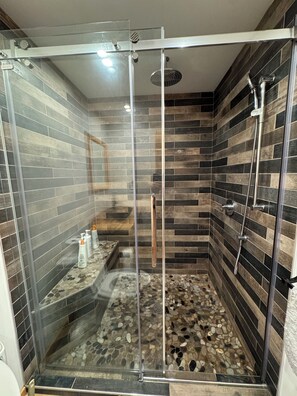 Une douche entièrementClose en verre, avec un sol recouvert de petits galets et un mur décoré avec un motif en bois.