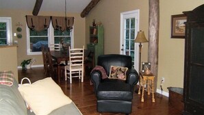 Un salon chaleureux avec un fauteuil en cuir, un coin repas avec des chaises en bois et un lustre.