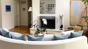 Un salon moderne avec un canapé d’angle blanc, une cheminée et un panneau décoratif mural.