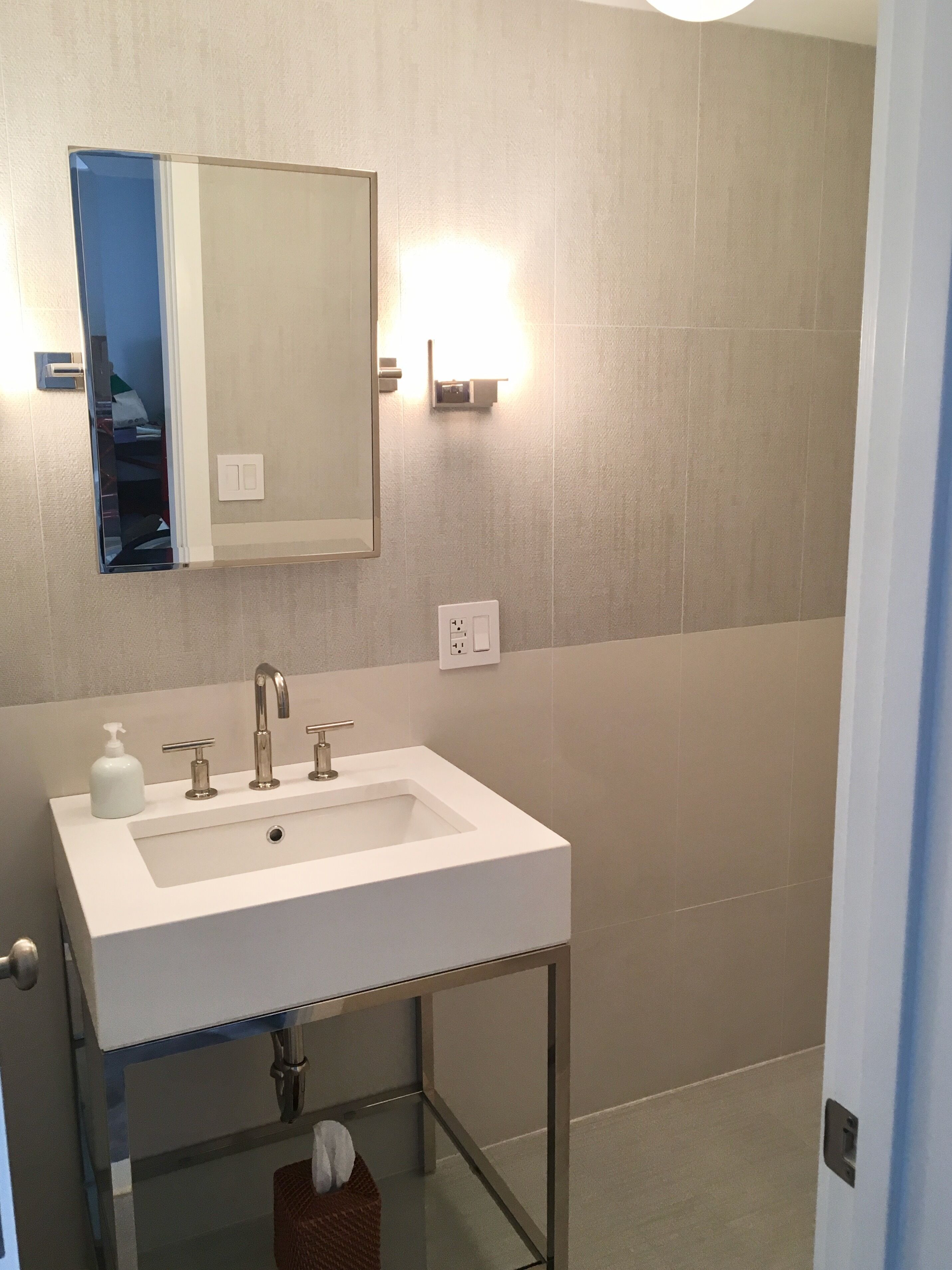 A modern bathroom with a white sink, a mirror, and a glass shelf below.