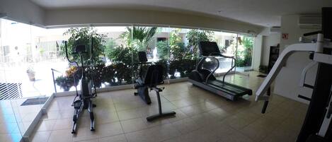 A gym with treadmills and exercise bikes, large windows with a view of greenery outside.