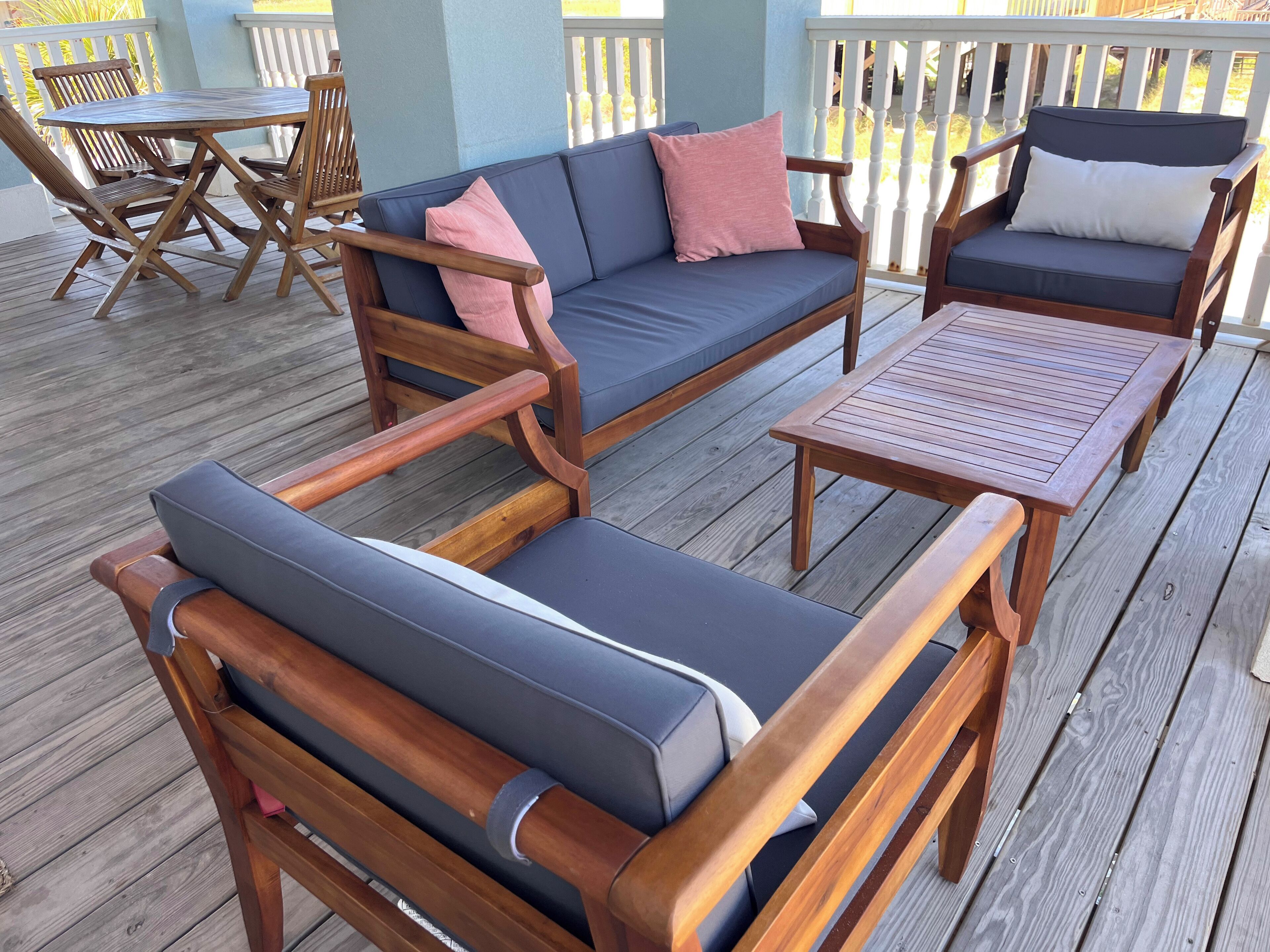 Una terraza de madera con un sofá, sillas, una mesa y una barandilla.